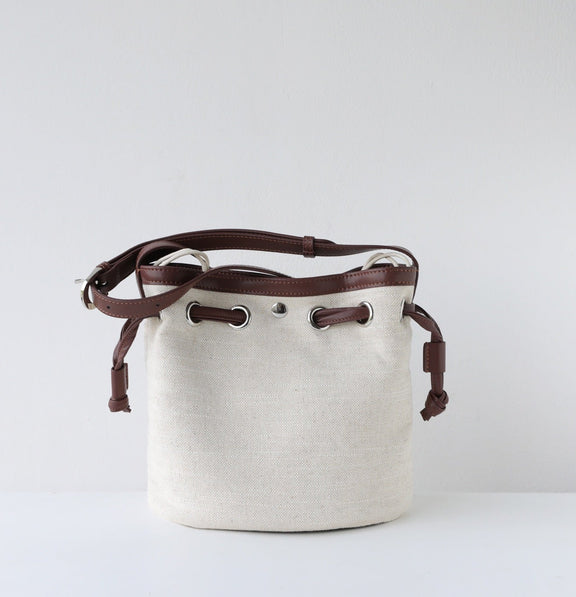 White bucket bag with brown leather straps on a light gray background