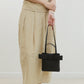 Person holding a black handbag with a bow detail against a white background, wearing a beige outfit.